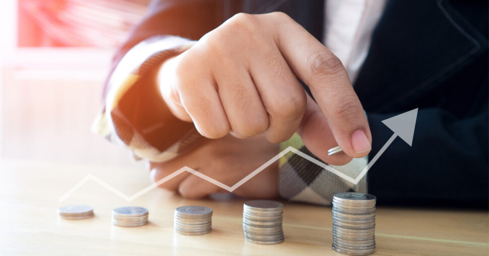 Hand stapelt Münzen mit wachsendem Pfeil im Hintergrund.