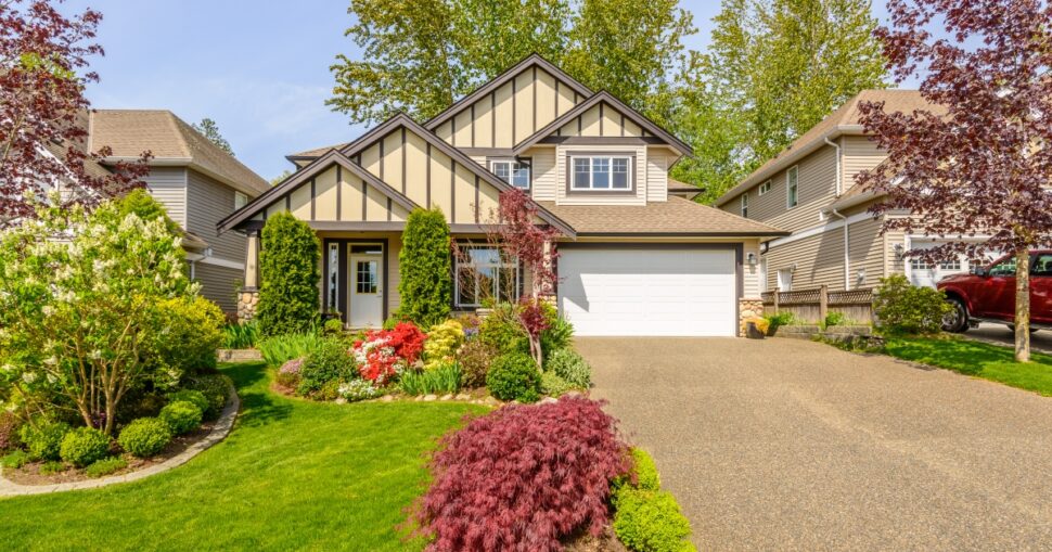 Einfamilienhaus mit gepflegtem Garten, bunter Blumenpracht und grünem Rasen im Vordergrund.