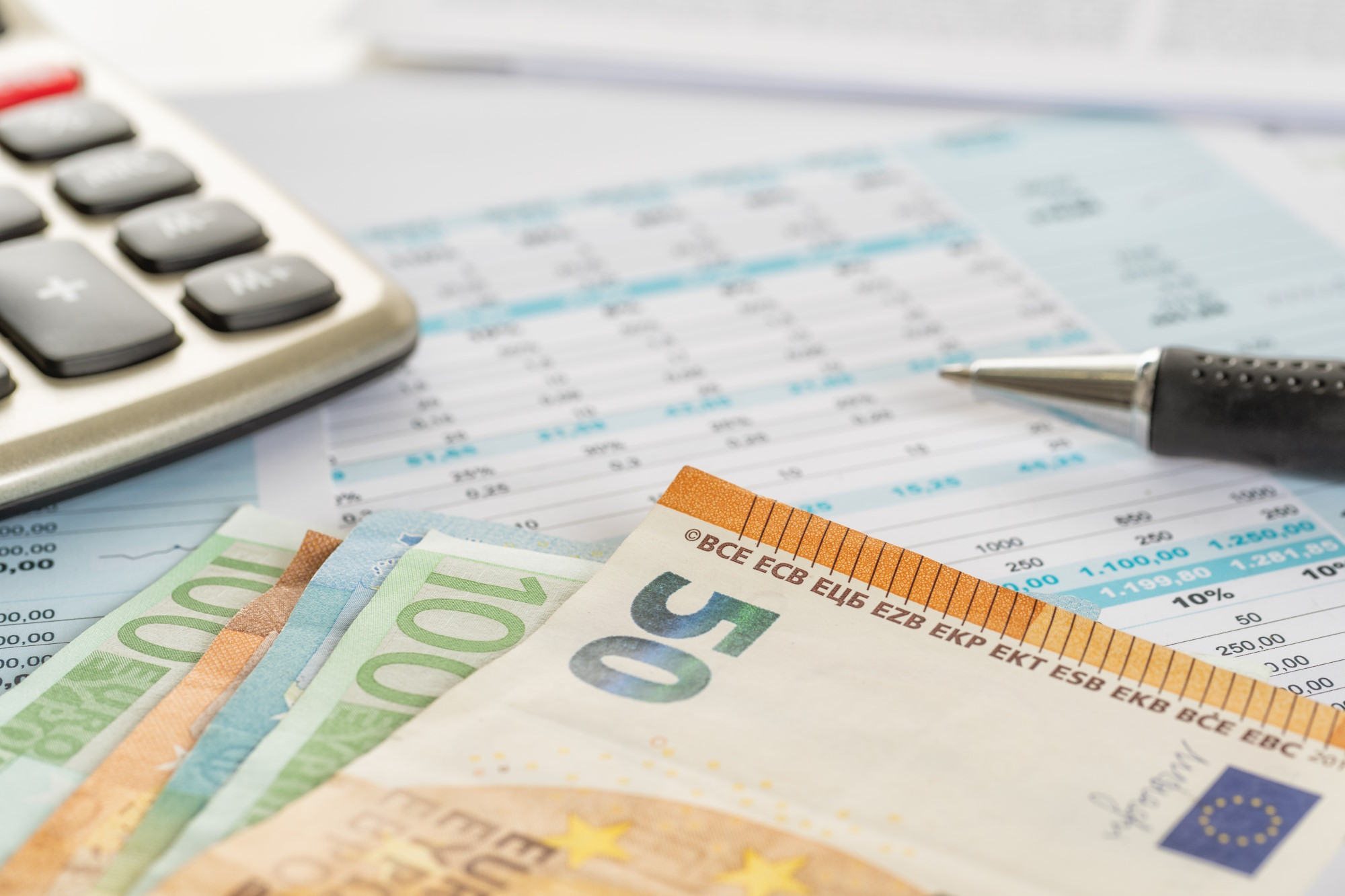 Taschenrechner, Euroscheine und ein Stift auf einer Finanzübersicht.