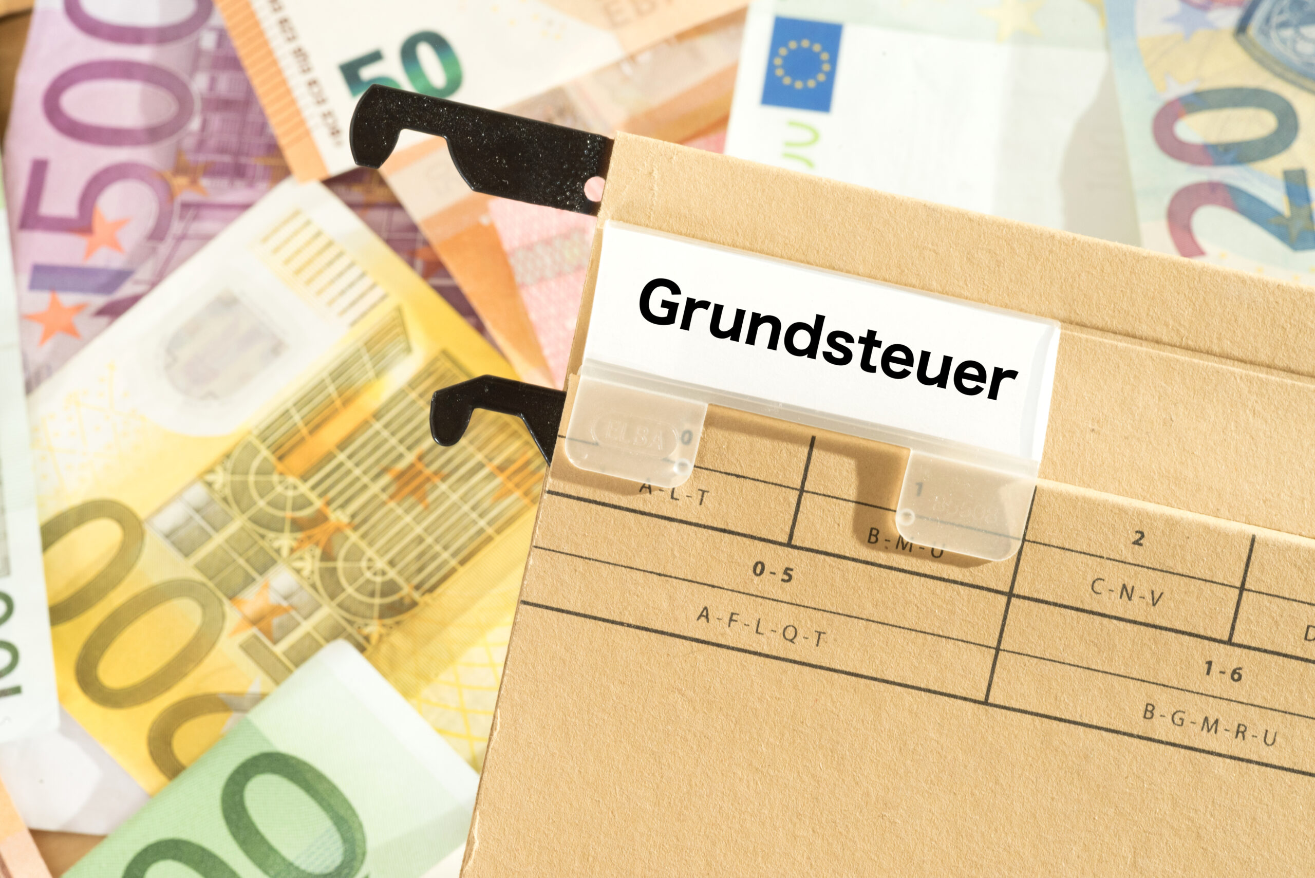 Ordner mit der Aufschrift "Grundsteuer" auf Euro-Banknoten liegend.